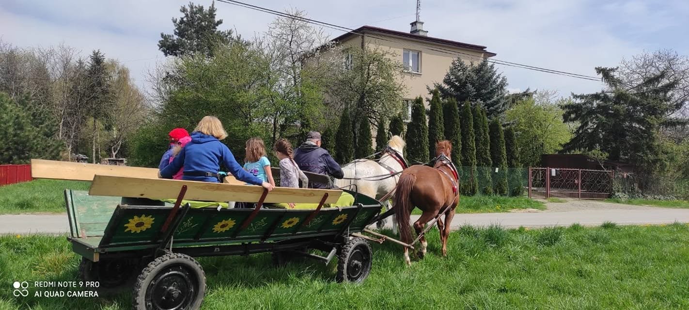 Dzieci na zielonym wozie taborowym zaprzężonym w dwa konie podczas przejażdżki po Mogile